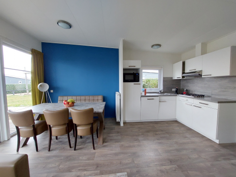 Cocina de lodge moderna con mesa de comedor, sillas de cuero, pared azul y luz natural desde la terraza.