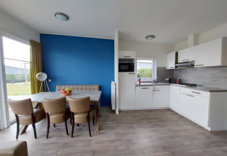 Cocina de lodge moderna con mesa de comedor, sillas de cuero, pared azul y luz natural desde la terraza.