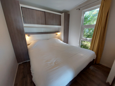 Dormitorio en una cabaña con cama grande, armarios de madera y ventana grande con vista a la naturaleza.