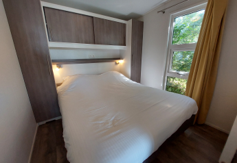 Schlafzimmer in einer Lodge mit großem Bett, Holzschränken und Blick ins Grüne durch das Fenster.