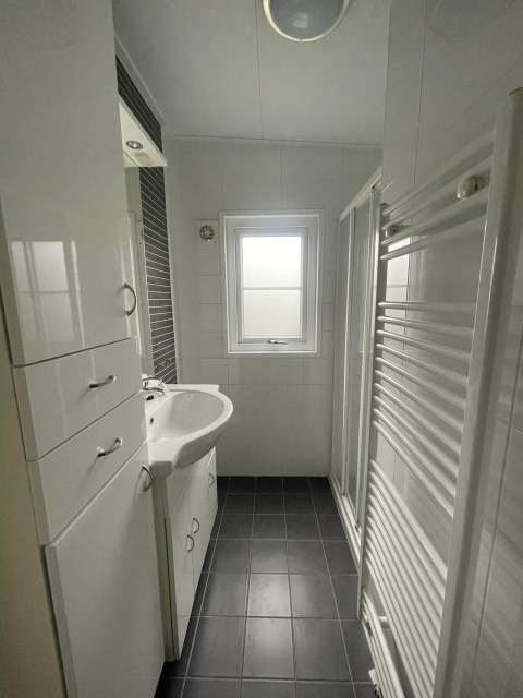 Lichte, moderne badkamer in Comfort Lodge met zwarte tegels, witte kasten en een raam.