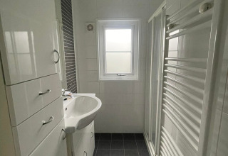 Lichte, moderne badkamer in Comfort Lodge met zwarte tegels, witte kasten en een raam.