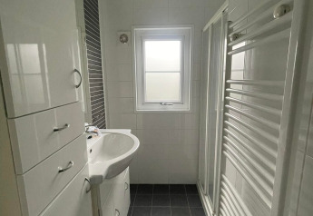 Lichte, moderne badkamer in Comfort Lodge met zwarte tegels, witte kasten en een raam.