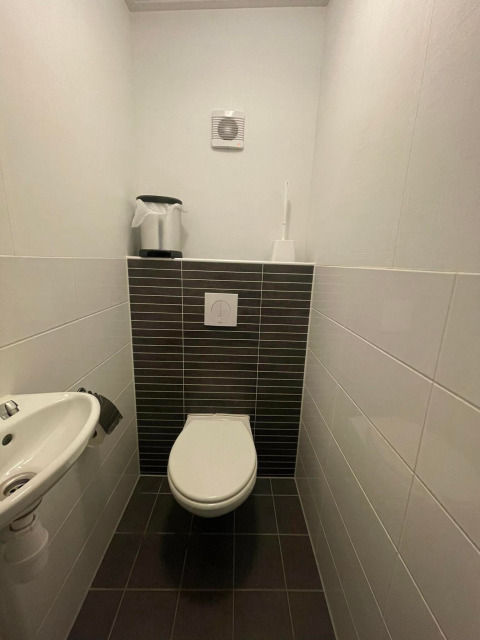 Baño moderno en Comfort Lodge - Dogs allowed, con inodoro suspendido y lavabo pequeño en baldosas oscuras.