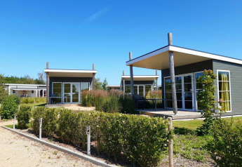 Moderni bungalow glamping con ampie vetrate e terrazze, immersi nel verde sotto un cielo limpido.