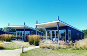 Dos lodges modernos con techos planos y grandes ventanas, rodeados de hierbas altas y cielo azul claro.