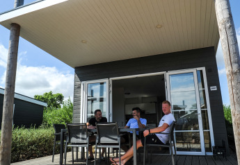 Tres hombres se relajan en la terraza de una Comfort Lodge en Kompas Camping Westende, Bélgica.