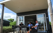 Tres hombres se relajan en la terraza de una Comfort Lodge en Kompas Camping Westende, Bélgica.