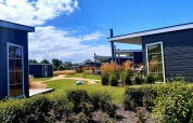 Cabañas modernas de glamping rodeadas de jardines y personas disfrutando de un día soleado al aire libre.