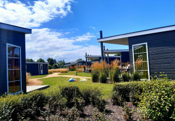 Modern glamping cabins with large windows, green landscaping, and people relaxing under a sunny sky.