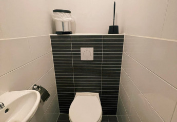 Baño moderno en Comfort Lodge con inodoro de pared, azulejos negros y pequeño lavabo de esquina.