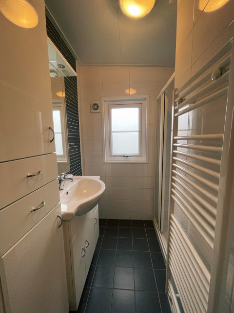 Moderne, compacte badkamer in Comfort Lodge met lavabo, kasten, raam en een verwarmd handdoekenrek.