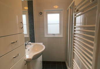 Moderne, compacte badkamer in Comfort Lodge met lavabo, kasten, raam en een verwarmd handdoekenrek.
