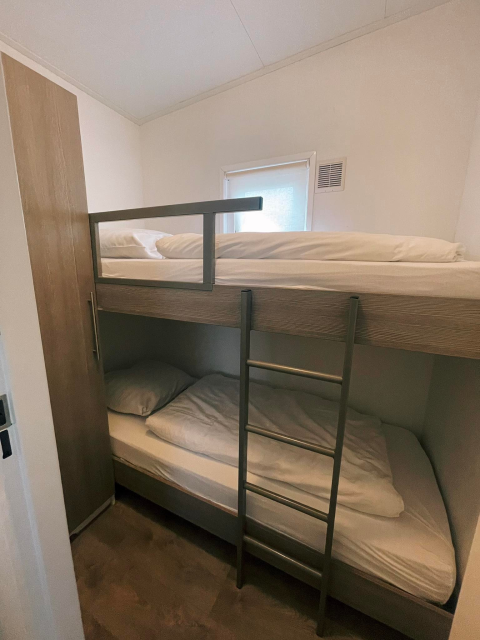 Kamer in Comfort Lodge met houten stapelbedden, compacte indeling en klein raam dat licht binnenlaat.