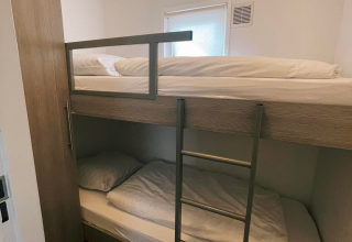 Kamer in Comfort Lodge met houten stapelbedden, compacte indeling en klein raam dat licht binnenlaat.