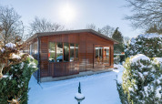 Sneklædt Veluwe lodge i Bungalowpark Het Verscholen Dorp, Holland, omgivet af vintertræer og buske.