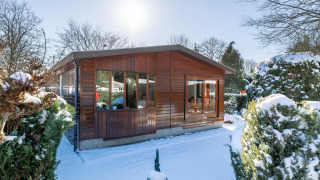 Veluwe lodge in de sneeuw bij Bungalowpark Het Verscholen Dorp, Nederland, omgeven door wintergroen.