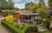 Charmerende Veluwe lodge ved Bungalowpark Het Verscholen Dorp, omgivet af grønne træer og hyggelig have.