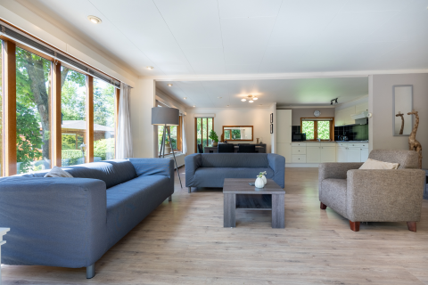 Lichte woonkamer met grote ramen, twee blauwe banken en modern interieur, Veluwe lodge, Het Verscholen Dorp.