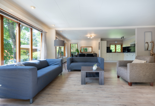 Lichte woonkamer met grote ramen, twee blauwe banken en modern interieur, Veluwe lodge, Het Verscholen Dorp.