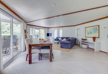 Luminoso salón-comedor con mesa, sofá y amplios ventanales en Veluwe Lodge, Het Verscholen Dorp, Países Bajos.