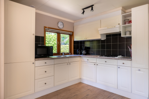 Moderne compacte Veluwe lodge keuken met witte kasten, zwarte tegels en raam in Nederland.