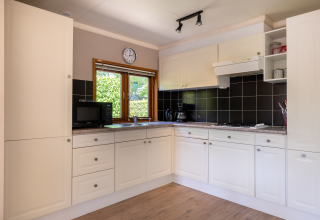Moderne compacte Veluwe lodge keuken met witte kasten, zwarte tegels en raam in Nederland.