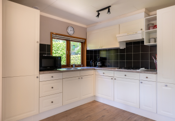 Modern, compact Veluwe lodge kitchen with white cabinets, black tiles, and bright window in the Netherlands.