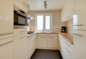 Cucina compatta moderna con armadi bianchi, forno integrato e macchina da caffè nella Veluwe lodge nei Paesi Bassi.