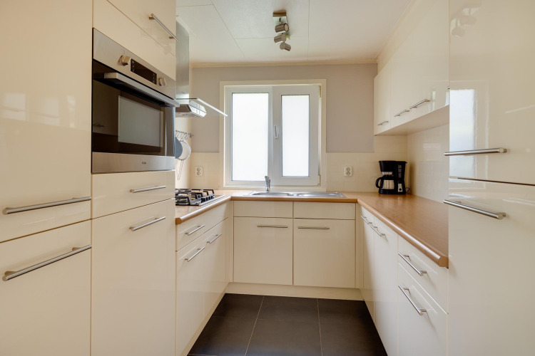 Cocina moderna y compacta con gabinetes blancos, horno empotrado y cafetera en Veluwe lodge, Países Bajos.