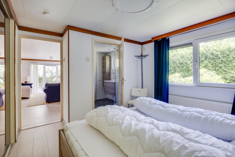 Slaapkamer in een Veluwe lodge bij Bungalowpark Het Verscholen Dorp met zicht op badkamer en woonkamer.