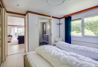 Slaapkamer in een Veluwe lodge bij Bungalowpark Het Verscholen Dorp met zicht op badkamer en woonkamer.
