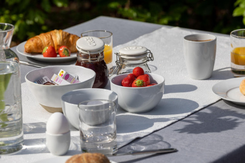 Buitenontbijt met croissants, aardbeien, ei, confituur en koffie op een wit tafellaken bij Veluwe lodge.