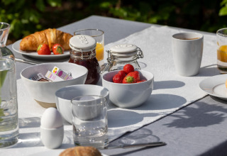 Buitenontbijt met croissants, aardbeien, ei, confituur en koffie op een wit tafellaken bij Veluwe lodge.