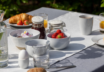 Petit-déjeuner en plein air avec croissants, fraises, œuf, confiture et café sur nappe blanche au Veluwe lodge.