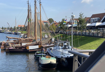 Barcos tradicionales amarrados junto a una orilla verde y casas en un puerto de los Países Bajos.