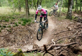 Twee mensen mountainbiken op een bospad bij de Veluwe lodge op Bungalowpark Het Verscholen Dorp in Nederland.