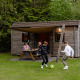 Familia disfrutando fuera de una cabaña de madera en Camping de Noetselerberg, niños juegan al fútbol.