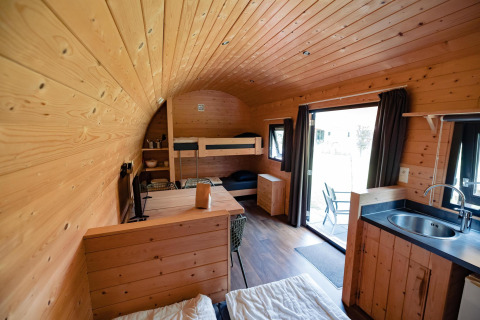 Intérieur en bois d’un lodge douillet avec lits superposés, coin cuisine et vue sur la terrasse extérieure.