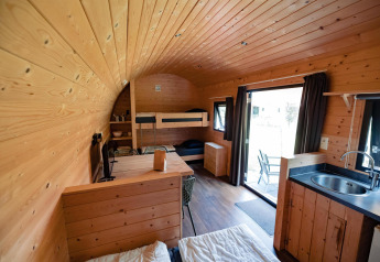 Interni in legno di un'accogliente lodge con letti a castello, angolo cottura e vista sulla terrazza esterna.
