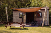 Photo de la Woodlodge au Camping the Noetselerberg, Pays-Bas, avec un lodge en bois, table de pique-nique et voile d'ombre.
