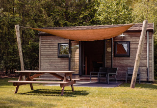 Photo de la Woodlodge au Camping the Noetselerberg, Pays-Bas, avec un lodge en bois, table de pique-nique et voile d'ombre.