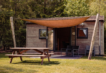 Foto van Woodlodge bij Camping the Noetselerberg in Nederland, met houten huisje, picknicktafel en schaduwdoek.