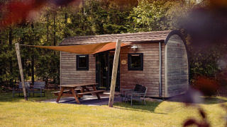 Woodlodge met picknicktafel en zitje buiten bij Camping de Noetselerberg in Nederland, midden in het groen.