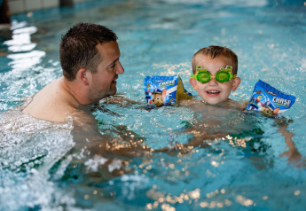 Erwachsener und Kind spielen lachend im Schwimmbad eines Glamping-Resorts, das Kind trägt Schwimmflügel.