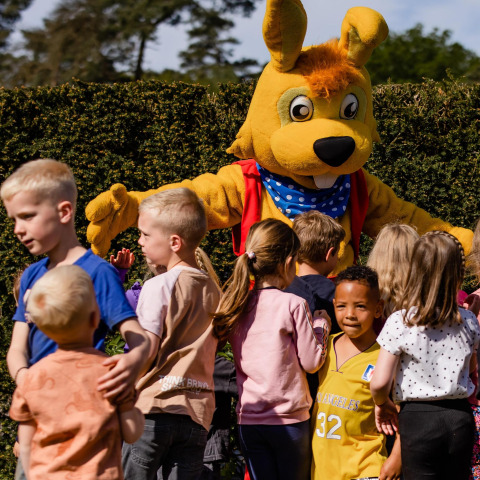 Des enfants jouent sur un site de glamping avec une mascotte de lapin géant par une journée ensoleillée.