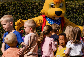 Kinderen spelen aan een glampingverblijf samen met iemand in een groot konijnenpak in de zon.