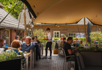 Buitenterras bij een glampingverblijf, gasten eten onder een zeildoek op een zonnige dag.