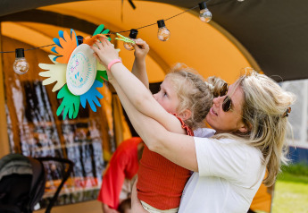 Una donna aiuta una bambina ad appendere decorazioni colorate su una catena luminosa in un glamping.