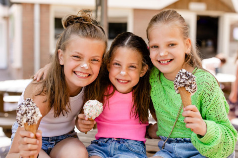 Drei fröhliche Mädchen genießen Eis vor einer Glamping-Unterkunft, lachend mit Eiscreme auf der Nase.